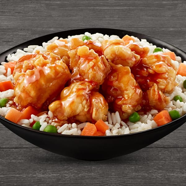 Sweet and sour chicken with white rice, peas, and carrots in a black bowl.