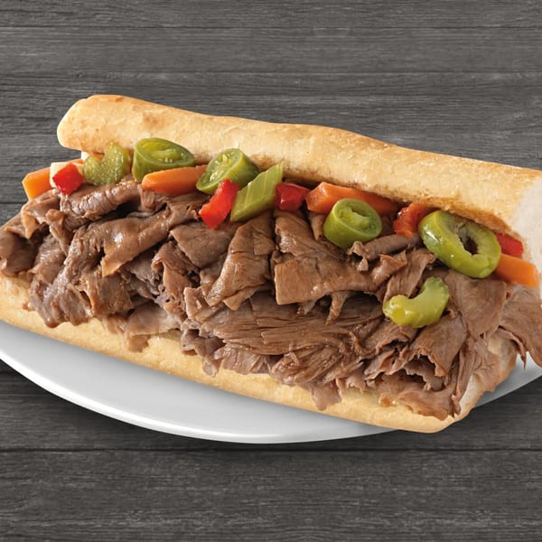 Brown's Chicken Italian beef sandwich with giardiniera on a white plate against a dark wood background.